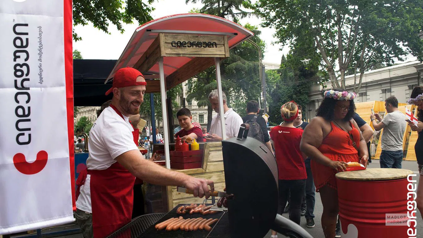 Сотрудник "Lider Food" жарит колбаски на улице