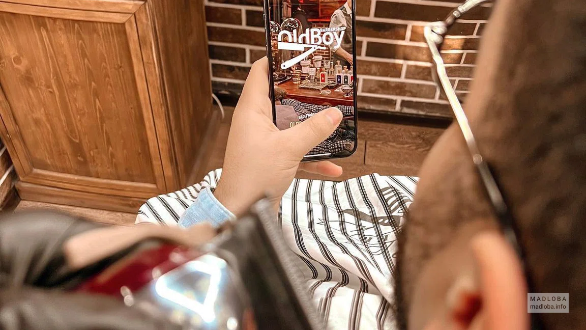Барбершоп OldBoy  клиент с мобильным телефоном в руках на экране которого логотип барбершопа OldBoy