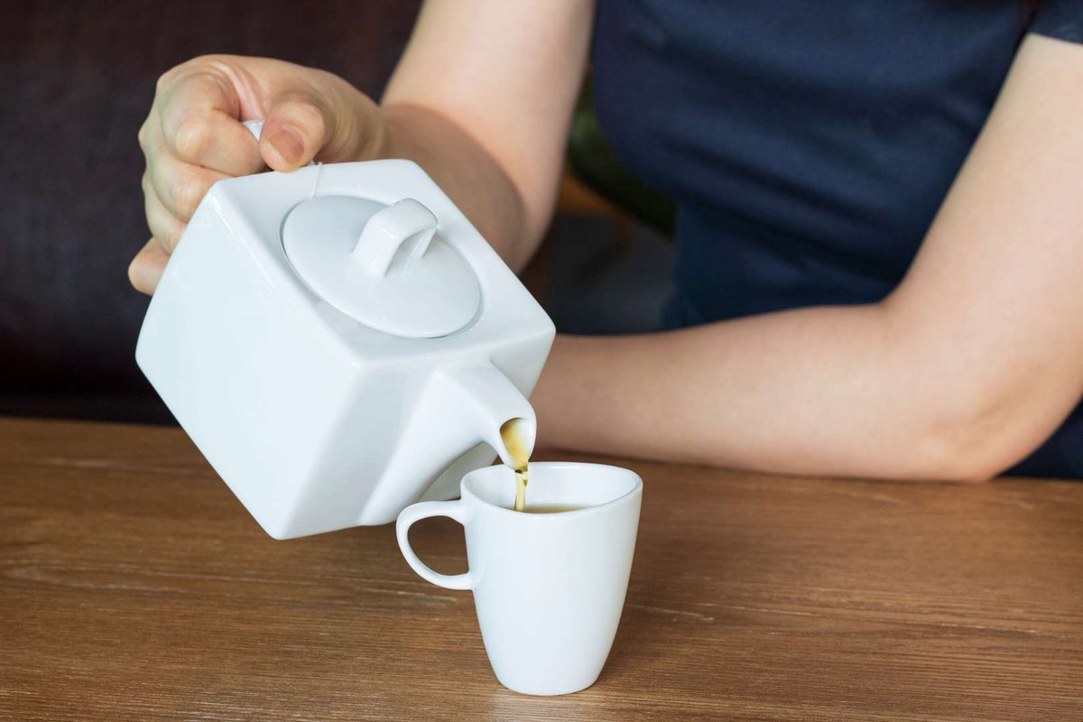 A girl drinks tea from a white teapot