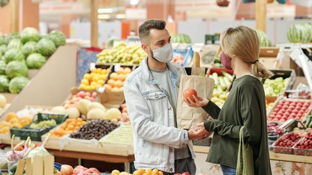 
								Молодая пара в тканевых масках стоит у прилавка и покупает продукты