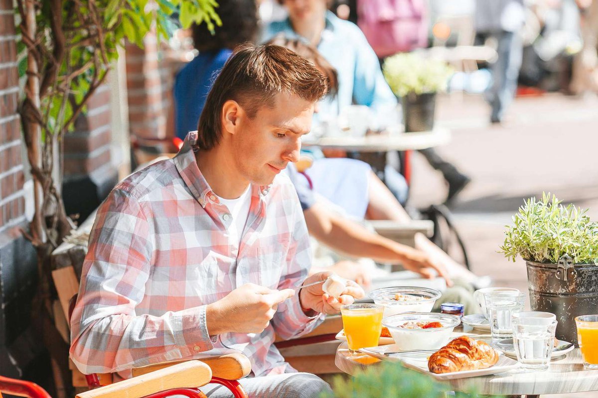 A young guy outside the cafe is having breakfast with healthy foods